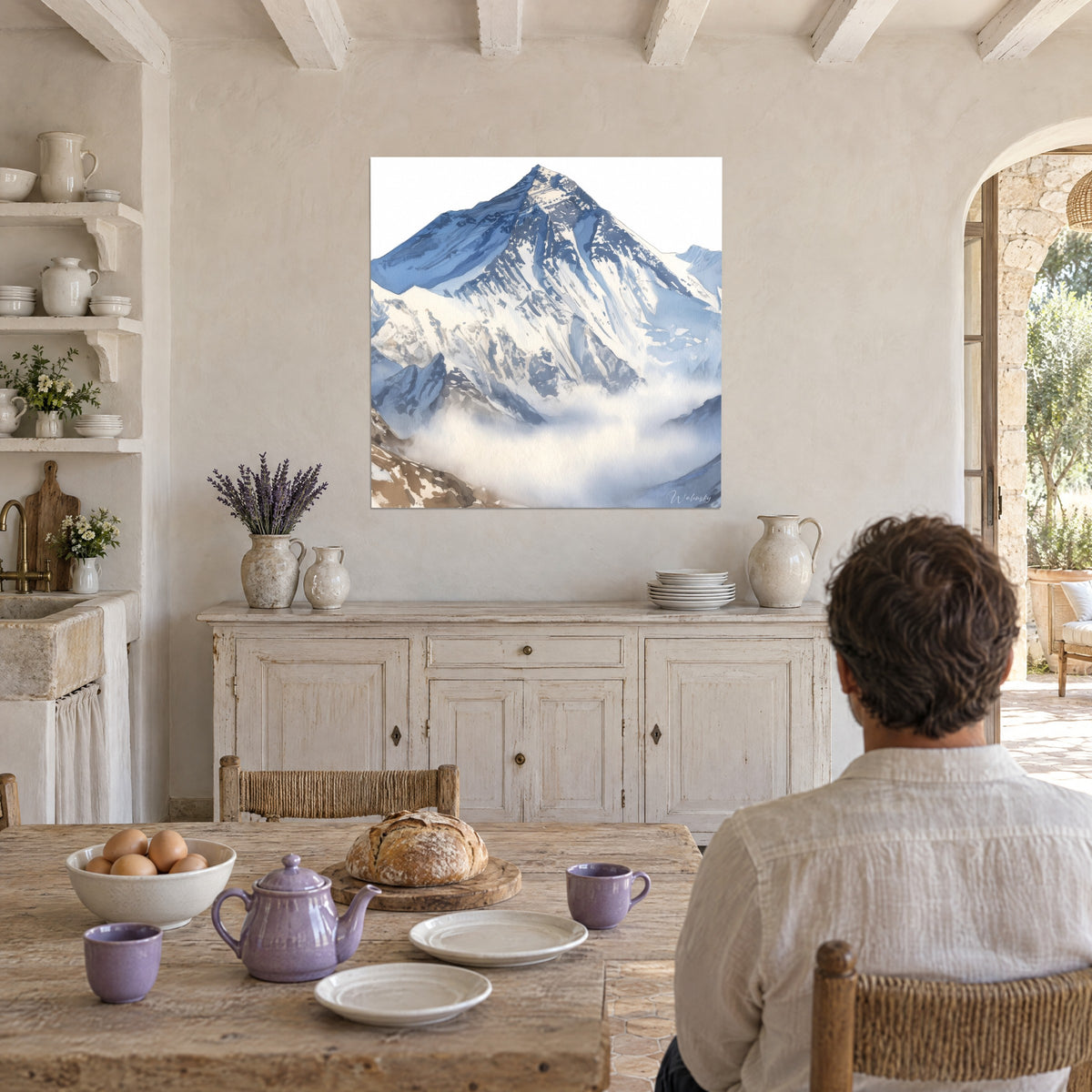 Cuadro montaña helada con aristas azul periwinkle y roca ocre, velo de bruma blanca, frente a una mesa de cocina de madera