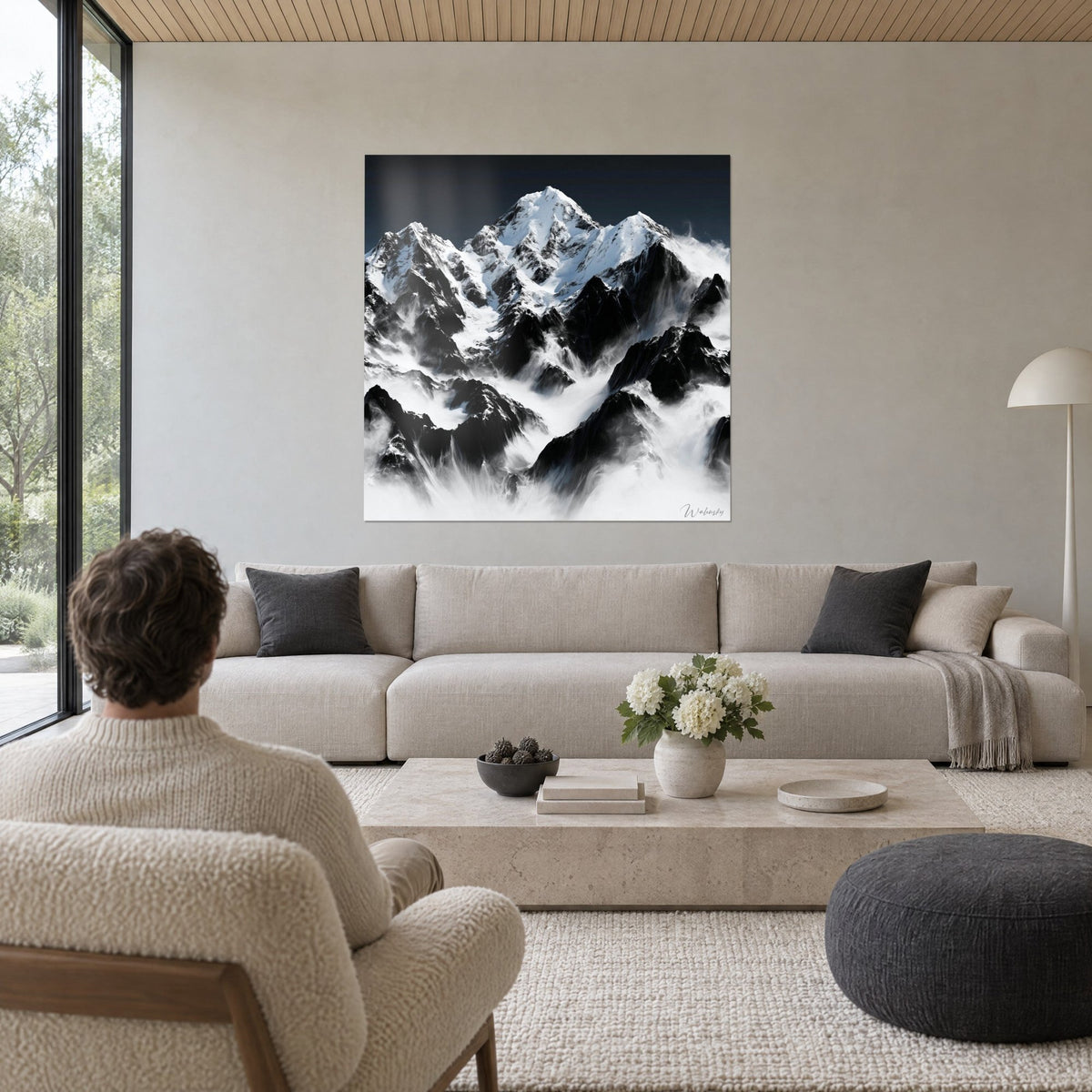 Gemälde schneebedeckter Gipfel mit schwarzen Felsen und weißem Nebel, Mann von hinten, über einem Sofa in einem hellen Wohnzimmer