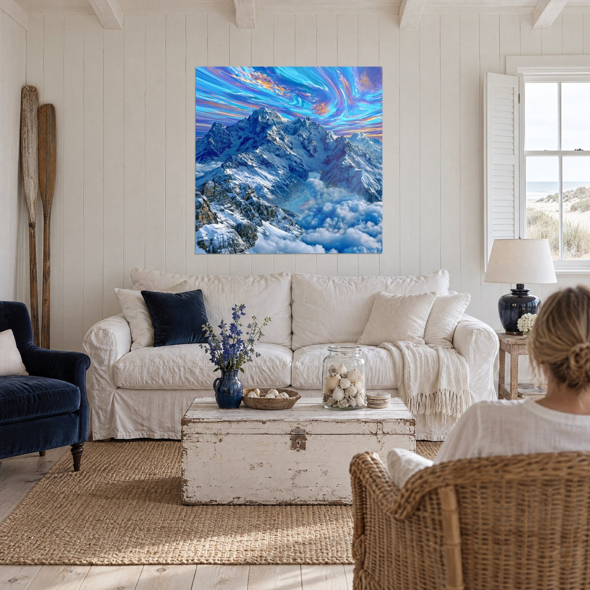Wall art snowy alpine peaks under a turquoise and orange sky, woman seen from behind, above a sofa in a bright living room