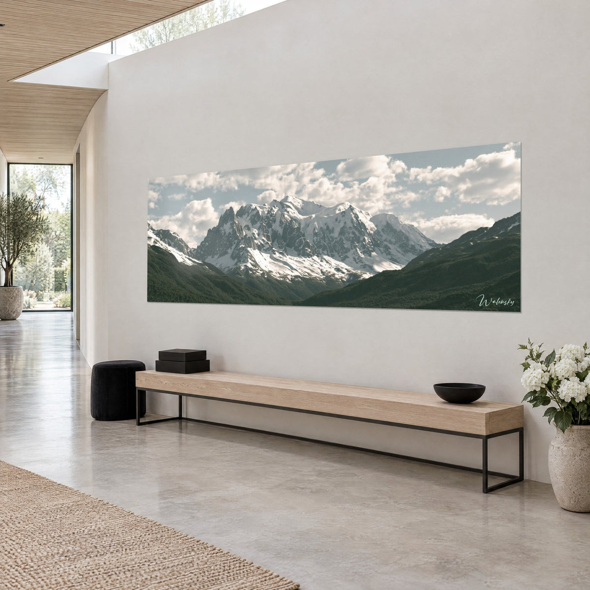 Gemälde mit vereisten Gipfeln und dunklen Graten, tannengrüne Hänge und blasser Himmel, aus einem Dreiviertelwinkel an einer weißen Wand