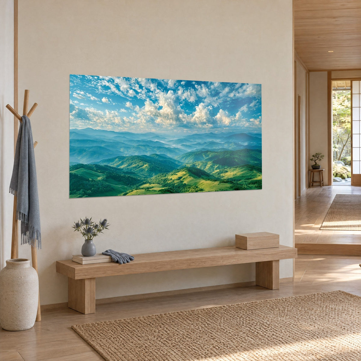 Quadro catena montuosa boschiva, cielo azzurro e nuvole avorio, appeso sopra una panca in legno chiaro in un ingresso