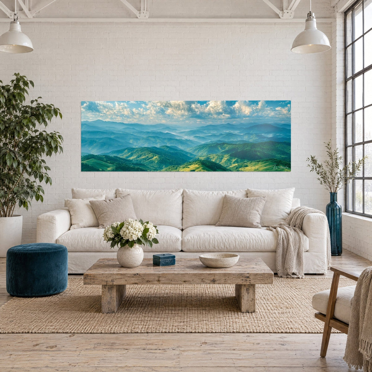 Gemälde Panorama aus smaragdgrünen und bläulichen Hügeln unter weißen Haufenwolken, Dunst im Hintergrund, über einem Sofa in einem hellen Wohnzimmer