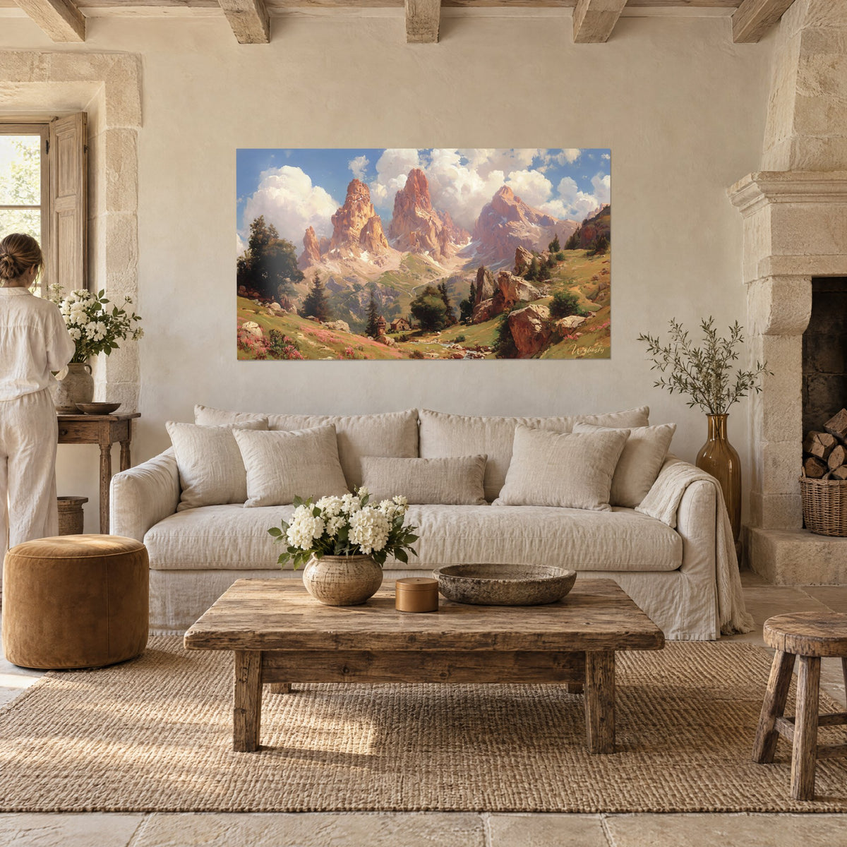 Wall art three pink rock peaks rising beneath large white clouds, green meadow, above a sofa in a bright living room