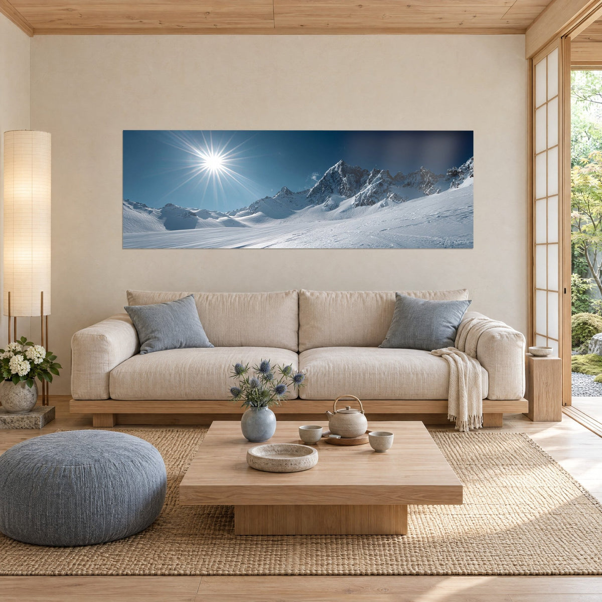 Wall art of snowy alpine peaks under a star-shaped sun, night-blue sky and grey ridges, above a sofa in a bright living room