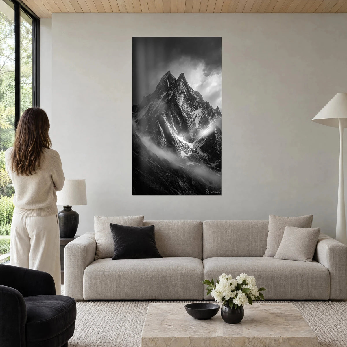 Schilderij rotstop in zwart-wit, witte kammen onder donkergrijze wolken, boven een bank in een lichte woonkamer