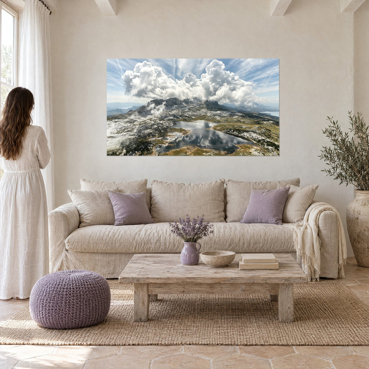 Wall art mountain lake reflecting clouds, white cumulus and blue sky, above a sofa in a bright living room