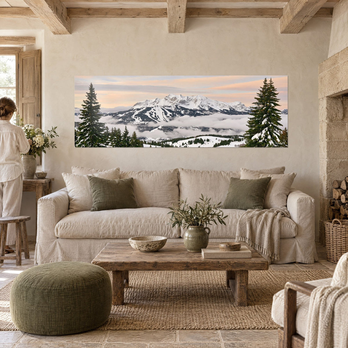 Tableau sapins enneigés encadrant un massif alpin, ciel rose pastel, nuages gris, au-dessus d'un canapé dans un salon lumineux