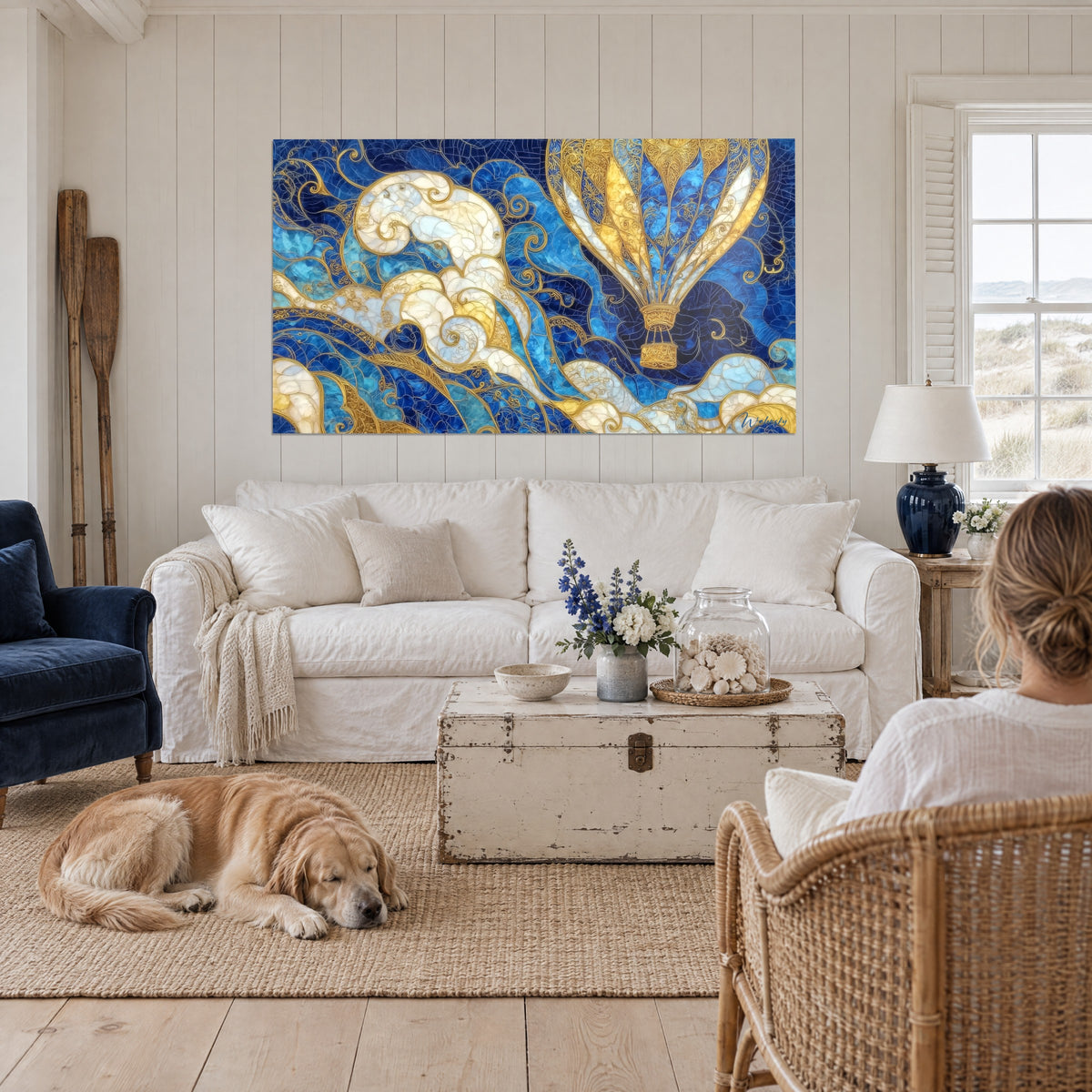 Gemälde Heißluftballon mit goldenem Filigran auf elfenbeinfarbenen und königsblauen Wolken, liegender Retriever, über einem Sofa in einem hellen Wohnzimmer