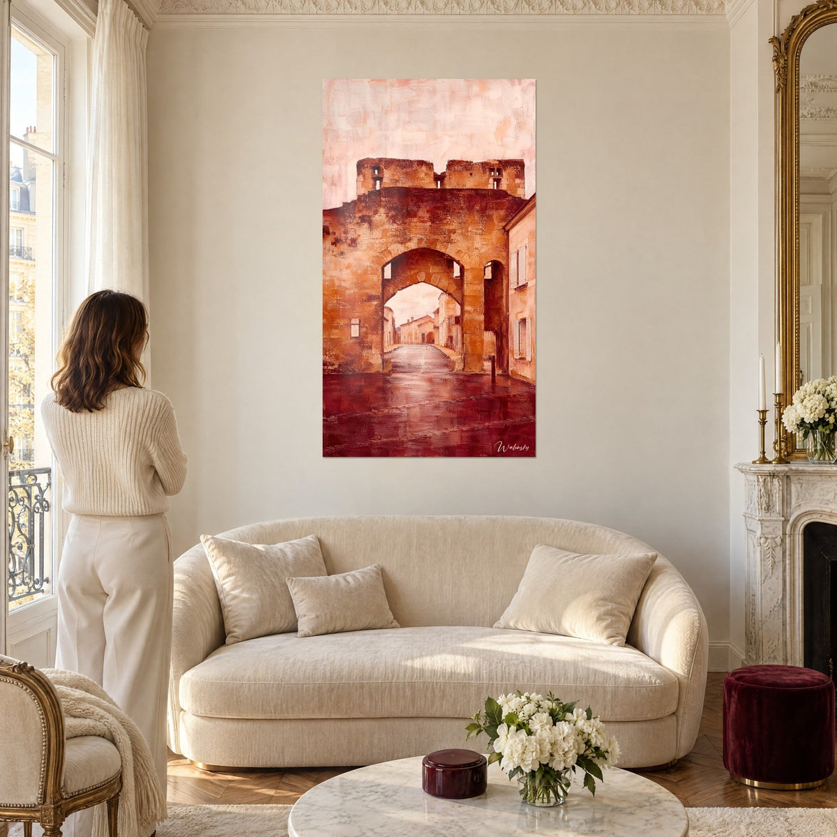 Cuadro puerta fortificada ocre con arco de piedra, cielo rosa pálido, mujer de espaldas, sobre un sofá en un salón luminoso