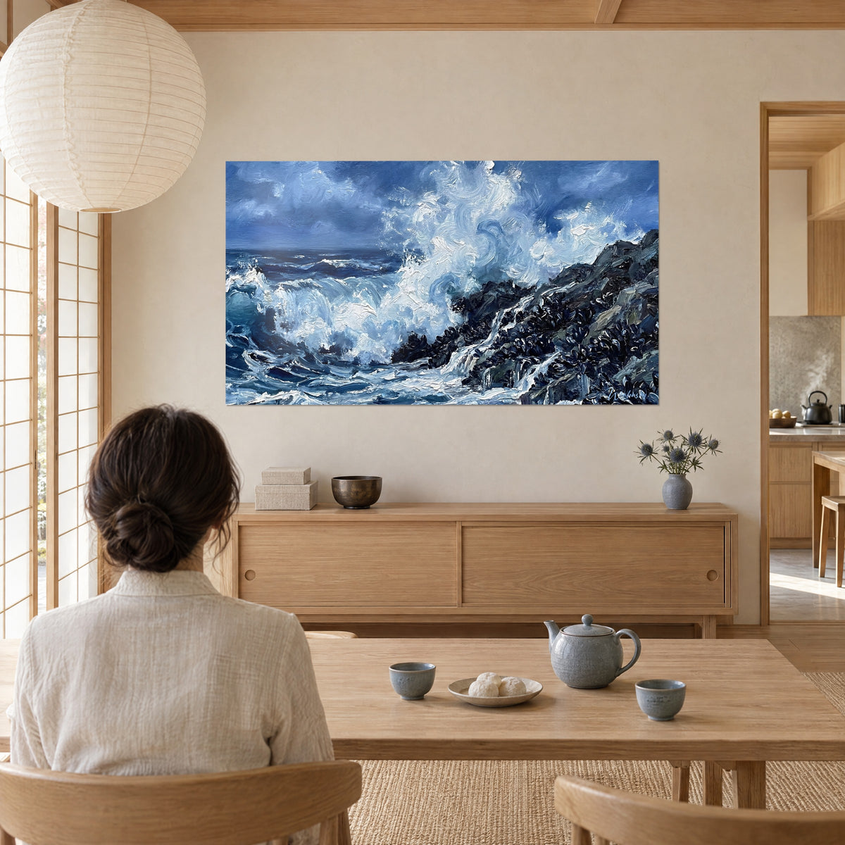 Tableau tempête océanique aux empâtements blancs et bleu nuit, roche sombre, devant un salon aux cloisons japonaises, femme de dos