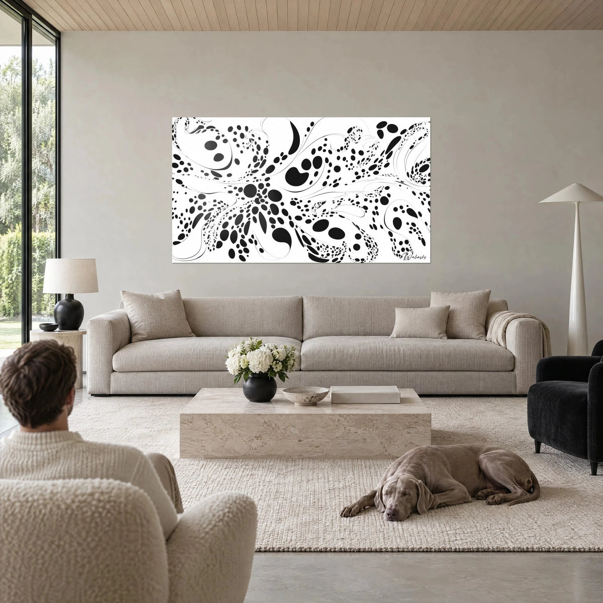 Schilderij met celpatroon van zwarte stippen op witte achtergrond, fijne krullen, man van achteren en hond, boven een bank in een lichte woonkamer