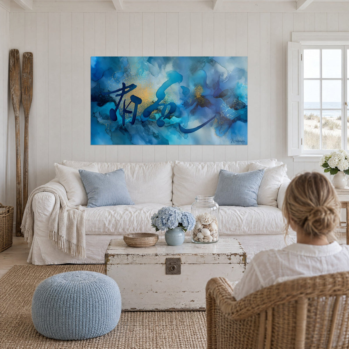 Quadro calligrafia indaco su nuvole turchesi e polvere d'oro, donna di spalle, sopra un divano in un soggiorno luminoso