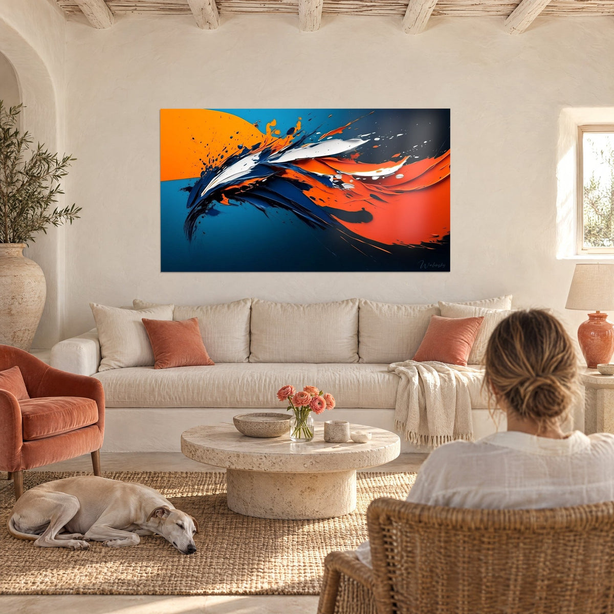 Wall art with orange and navy brushstrokes flung into splashes, woman seen from behind and a sleeping greyhound, above a sofa in a bright living room