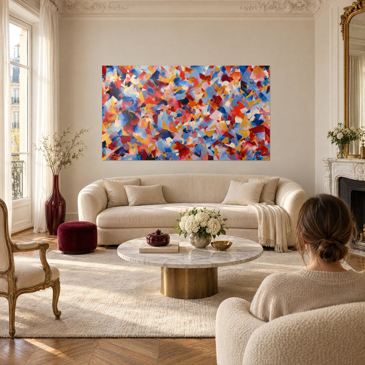 Tableau mosaïque abstraite de triangles rouges, bleus et dorés, une femme de dos, au-dessus d'un canapé dans un salon lumineux