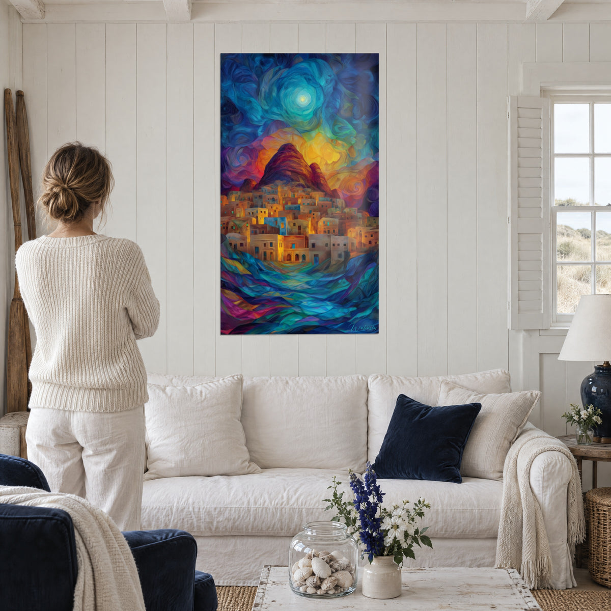 Wall art of an ochre rock city under a swirling blue and yellow sky, woman seen from behind, above a sofa in a bright living room