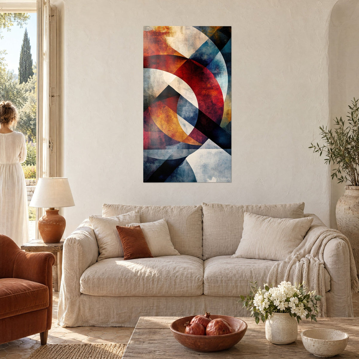 Wall art with intertwined circles in carmine red, streaked with ochre and steel blue, woman seen from behind above a sofa in a bright living room
