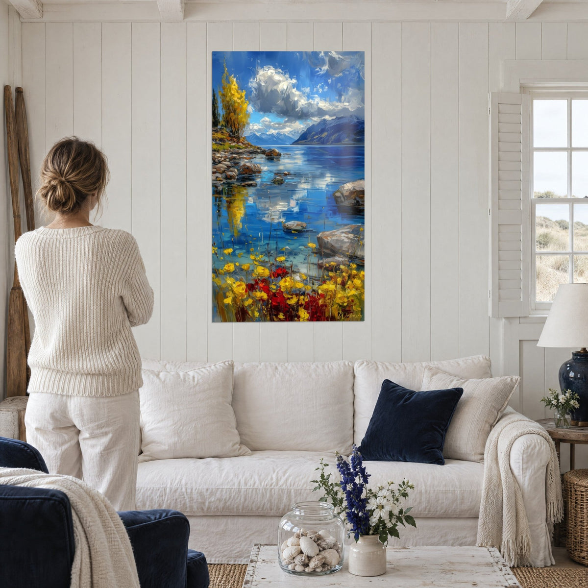 Schilderij alpenmeer met blauwe wateren en gele bloemen, pluizige wolken, verre bergen, boven een bank in een lichte woonkamer