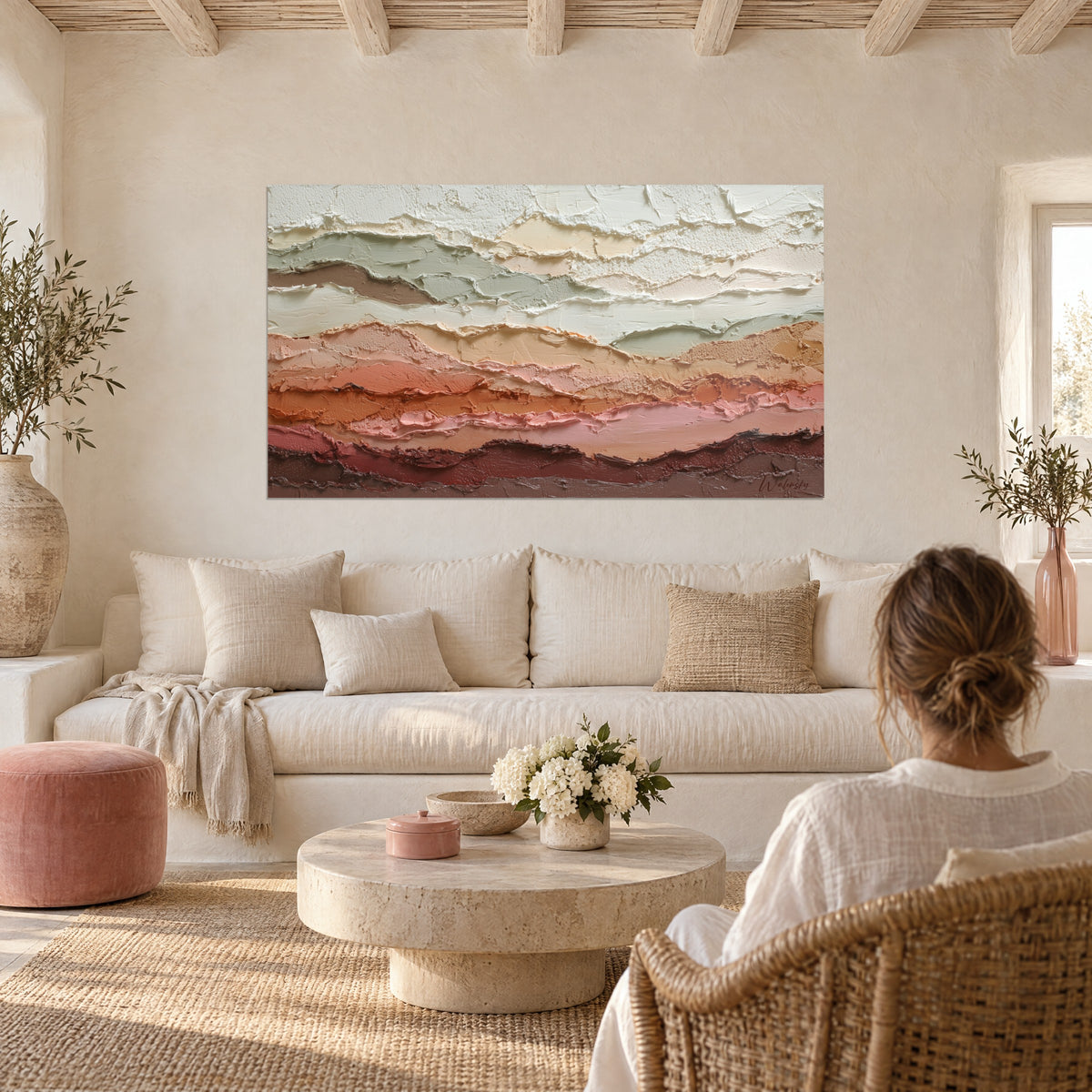 Quadro con spesse stratificazioni di pasta in salvia, ocra e rosa cipria, una donna di spalle sopra un divano in un soggiorno luminoso