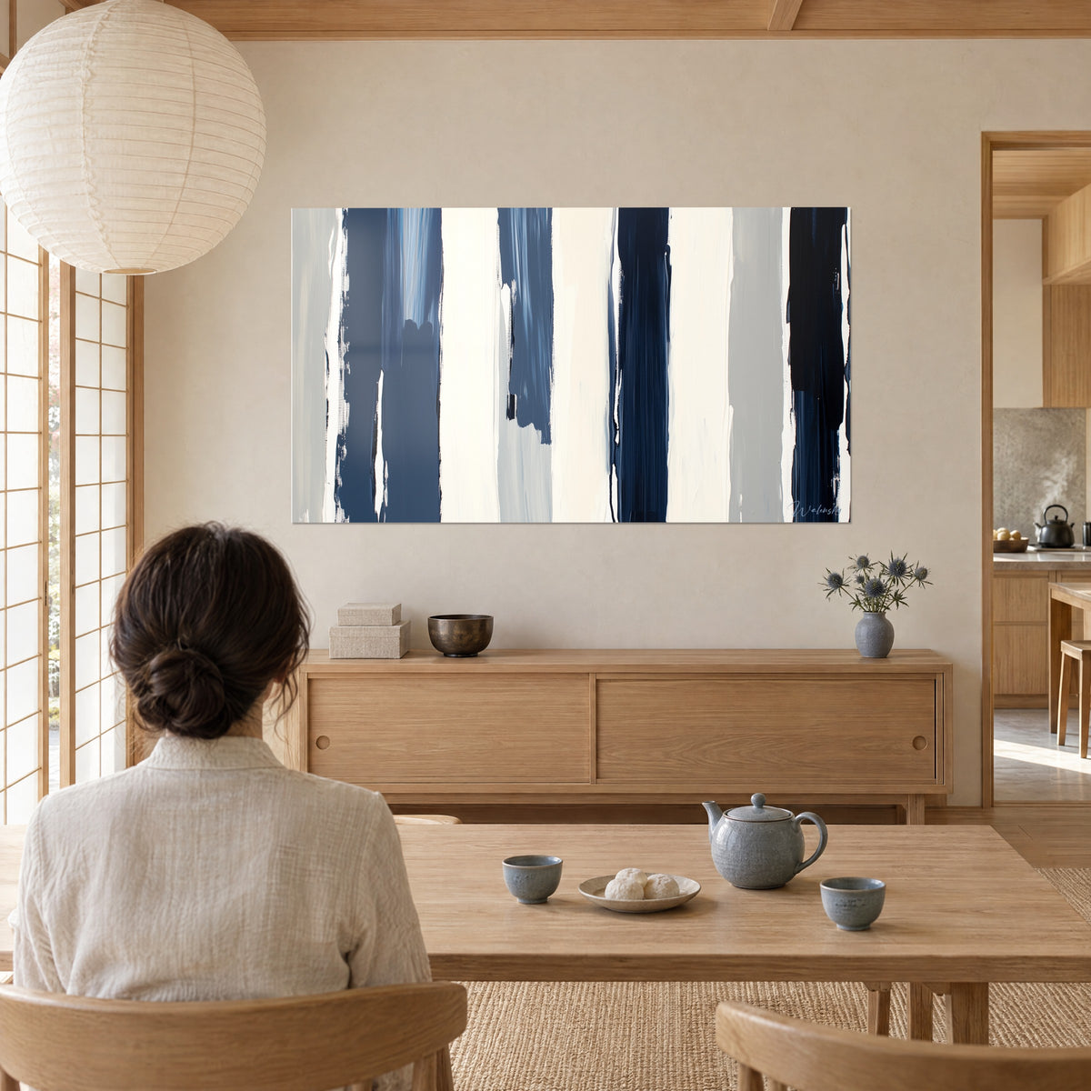 Wall art abstract canvas with broad blocks of steel blue and cream, brushstroke trails, facing a woman seen from behind near the tea