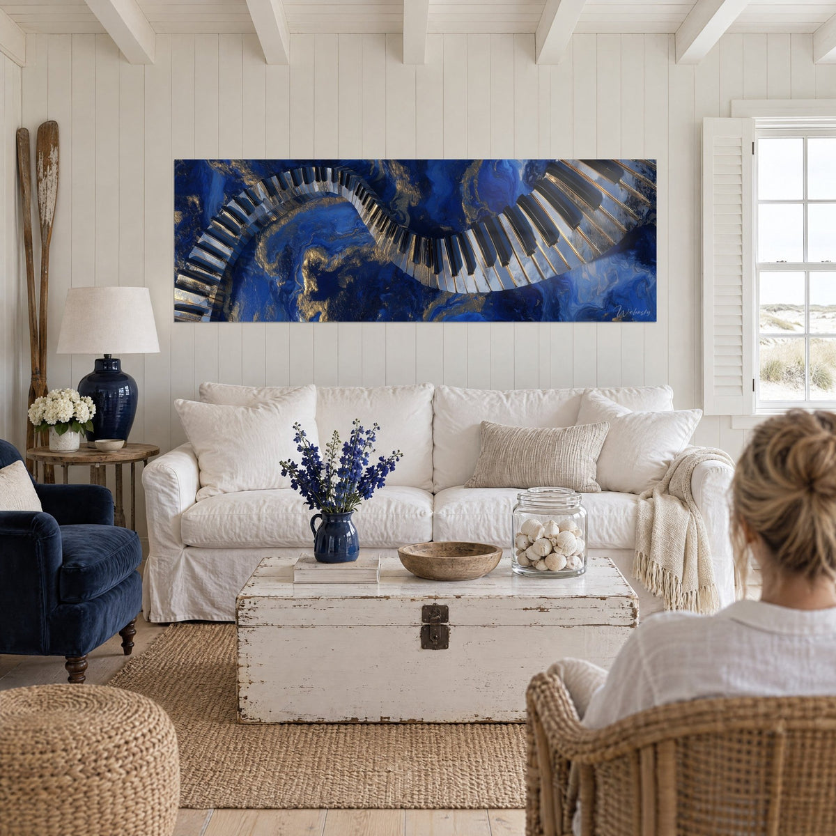 Schilderij pianotoetsenbord als golvend lint over marineblauwe en gouden marmering, twee vrouwen met hun rug naar de kijker, boven een bank in een lichte woonkamer