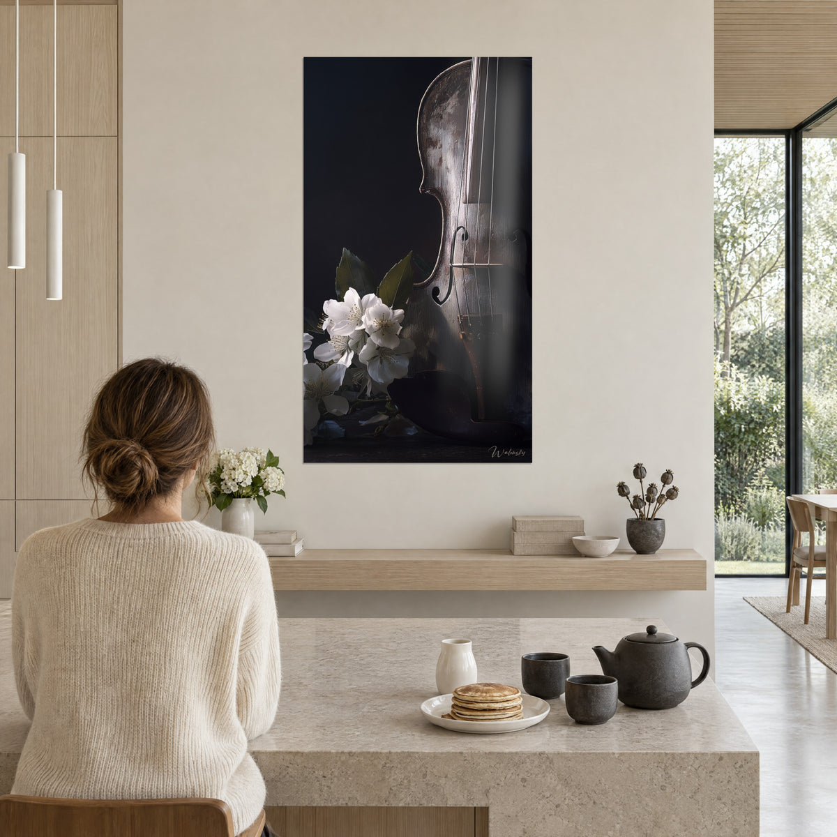 Wall art of a burnished violin body, taut strings and ivory flowers on a black background, woman in a cream sweater seen from behind near a kitchen island