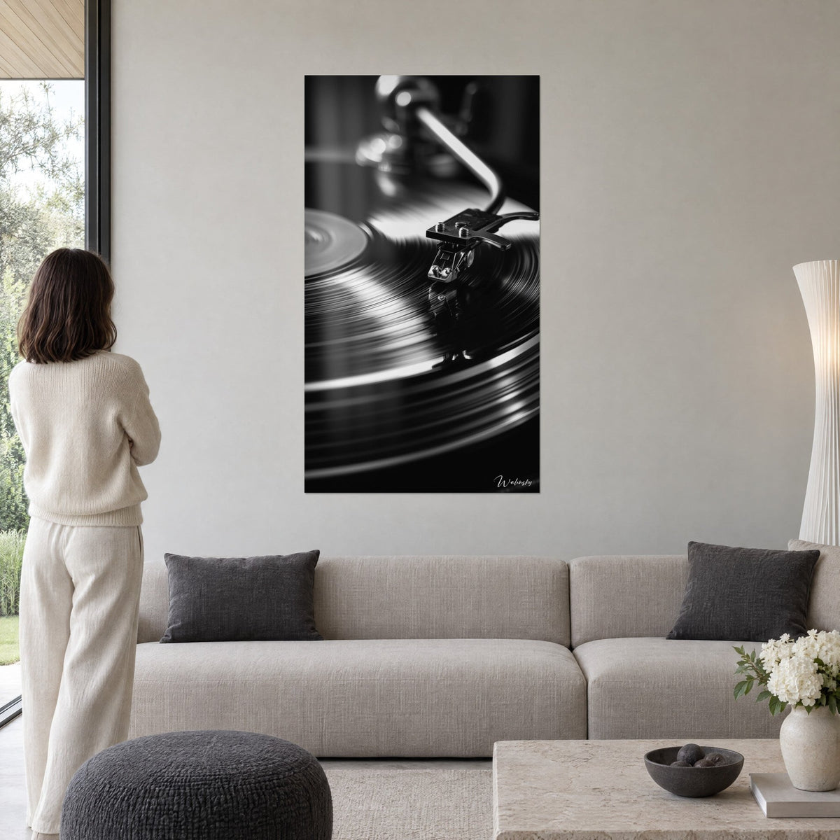 Wall art black and white vinyl turntable, silver grooves and chrome tonearm, woman seen from behind, above a sofa in a bright living room