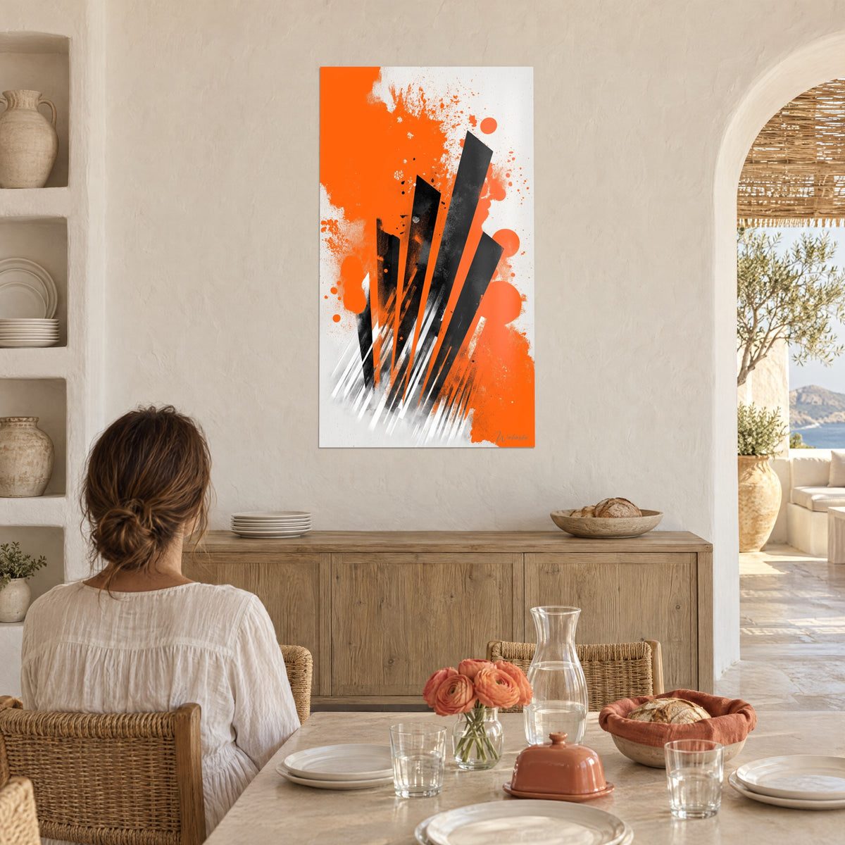 Wall art with an explosion of orange pigments, white and black streaks, woman seen from behind seated at a table in a vaulted open-plan kitchen