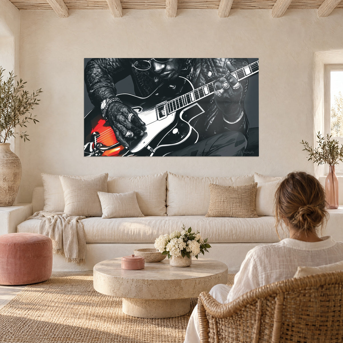 Schilderij van een gitarist in een zwart leren jack, ronde bril en zilveren ringen, oranjerode gitaar, boven een bank in een lichte woonkamer