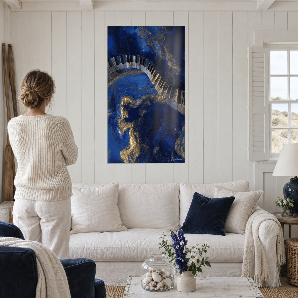 Wall art serpentine piano keyboard in midnight blue and gold marbling, woman seen from behind, above a sofa in a bright living room