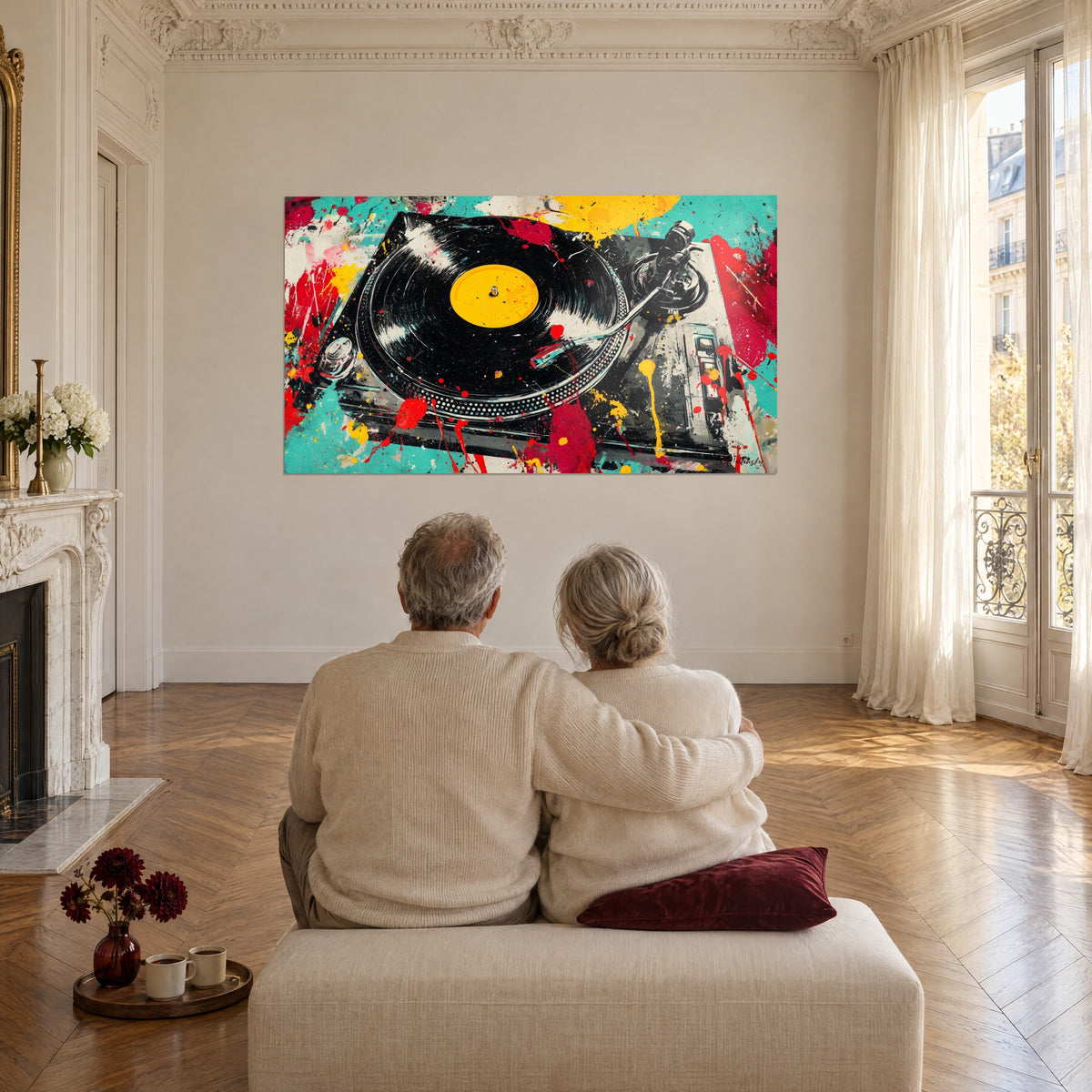 Πίνακας DJ πικάπ με πιτσιλισμένη ζωγραφική, τυρκουάζ, κόκκινο και κίτρινο, απέναντι από ένα ζευγάρι που κάθεται με την πλάτη σε κρεμ πουφ