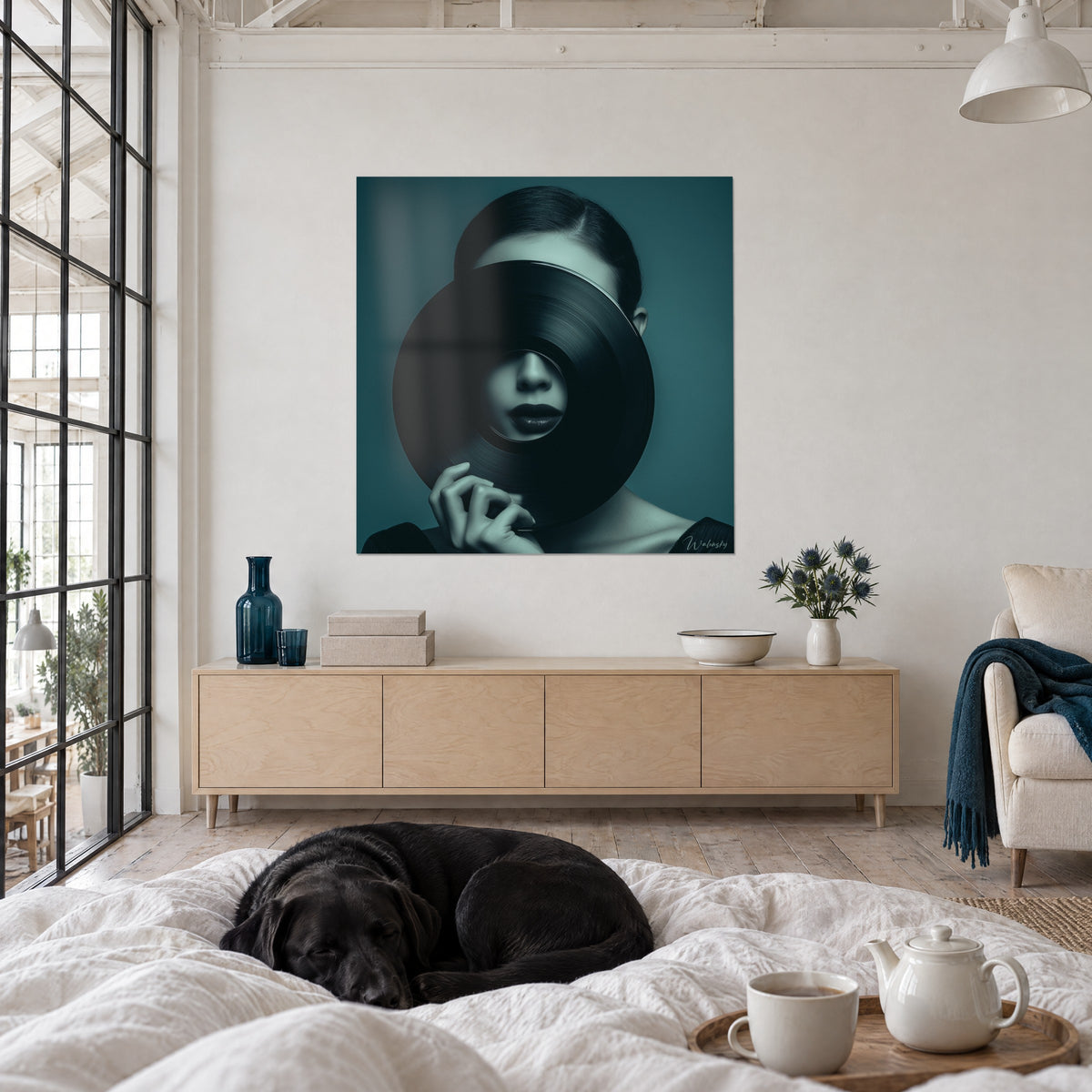 Schilderij Vrouw verscholen achter een zwarte vinylplaat, petrolblauw en lichtgroen, donkere lippen, boven een bed in een lichte slaapkamer