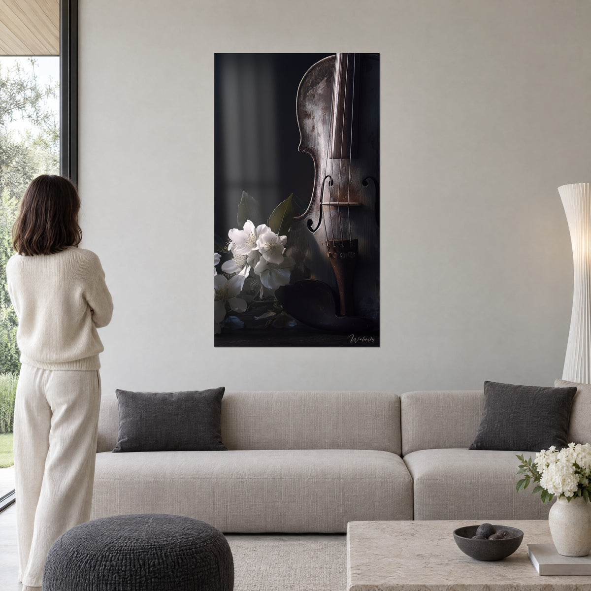 Wall art of an aged, patinated violin against a black background, white flowers and green leaves, woman seen from behind, above a sofa in a bright living room