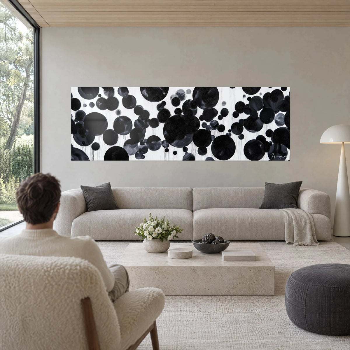 Wall art of black ink discs splashed with glittering specks on a white background, above a sofa in a bright living room