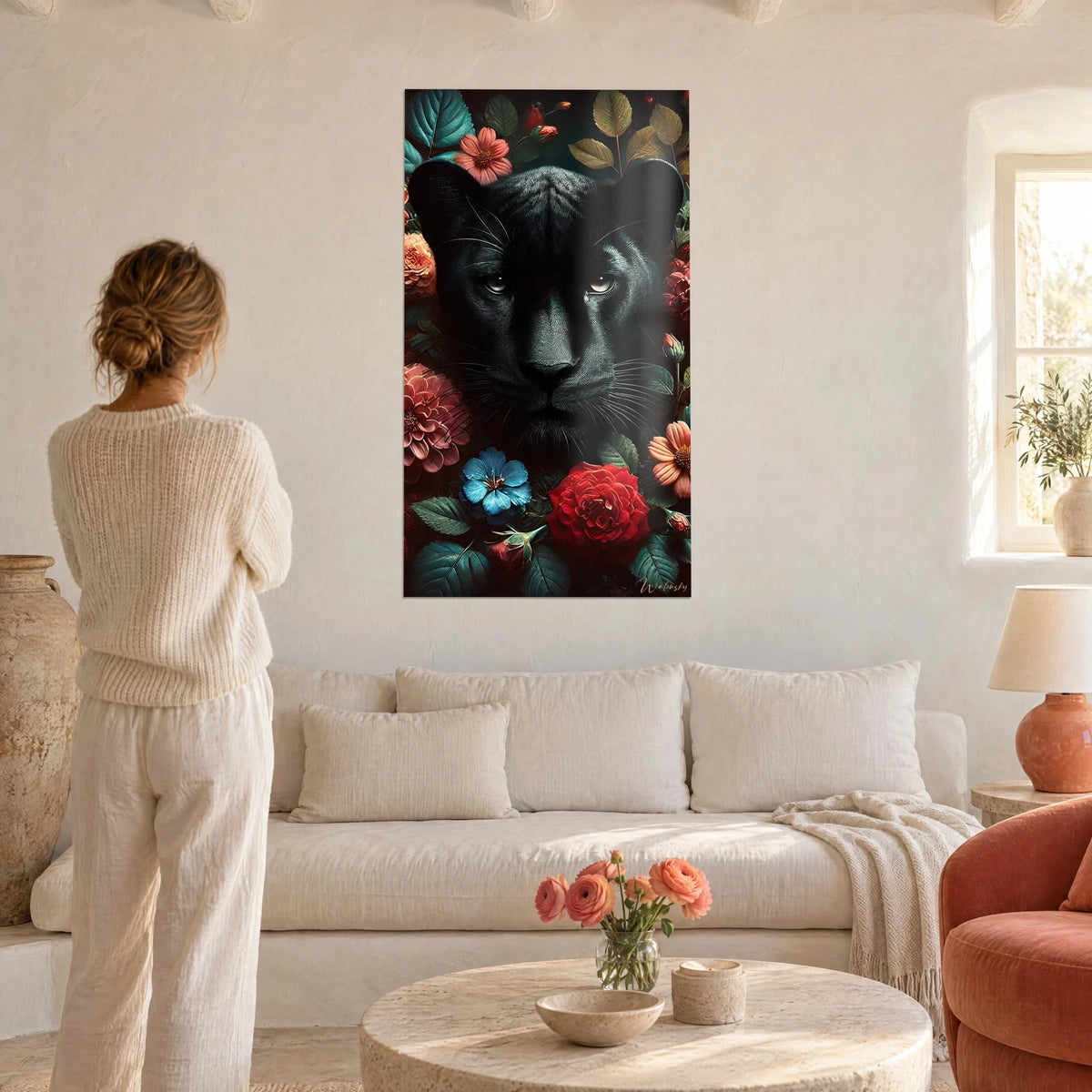 Gemälde schwarzer Panther mit hellen Augen, umgeben von roten Rosen und korallenfarbenen Blüten, über einem Sofa in einem hellen Wohnzimmer