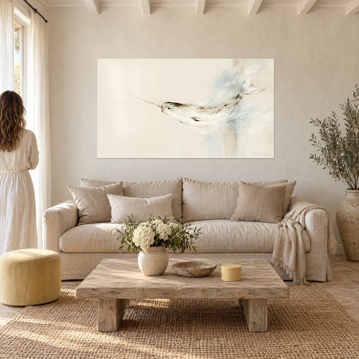 Wall art ivory and pastel blue narwhal, long slender tusk in the foam, couple seen from behind, above a sofa in a bright living room