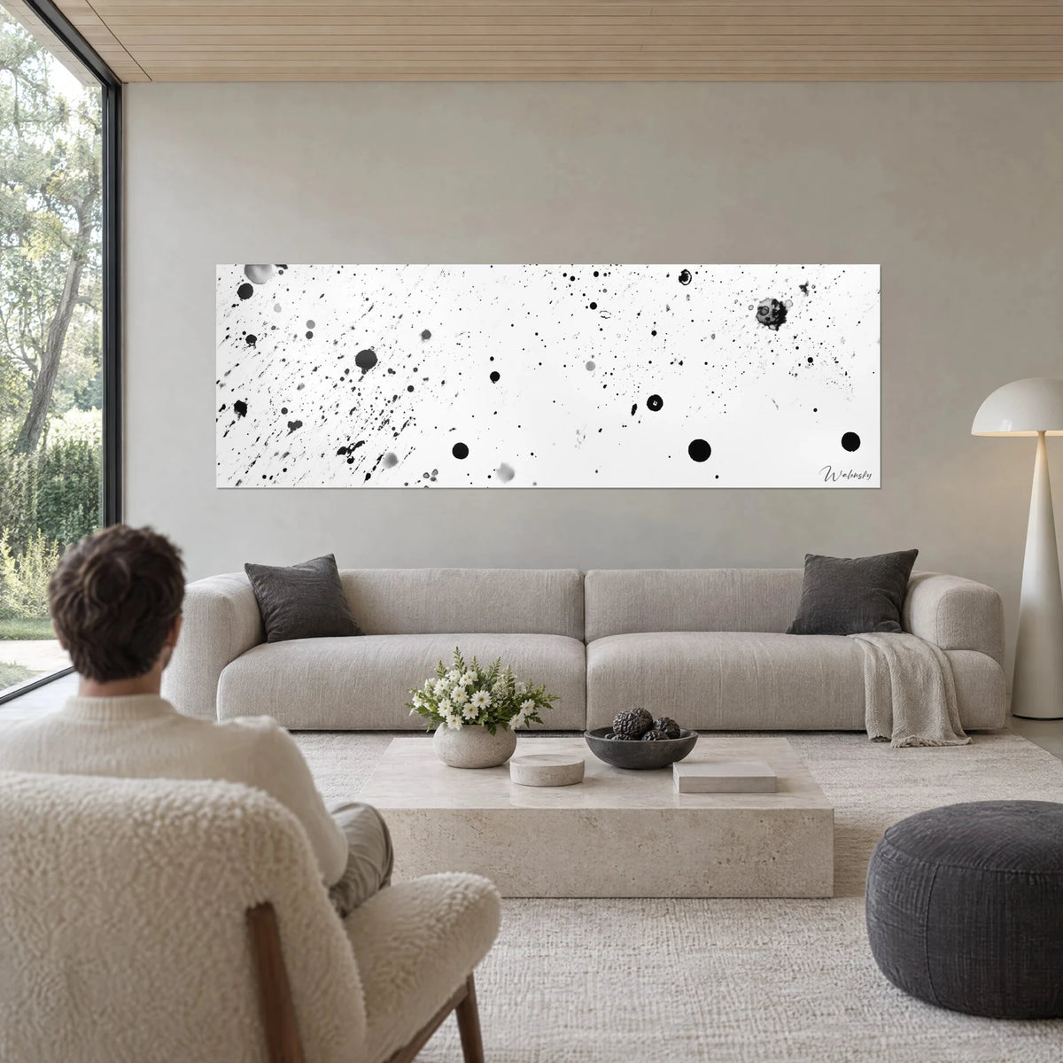 Gemälde mit schwarzen Tintenspritzern auf reinweißem Grund, feine Tropfen und breite graue Scheiben, über einem Sofa in einem hellen Wohnzimmer