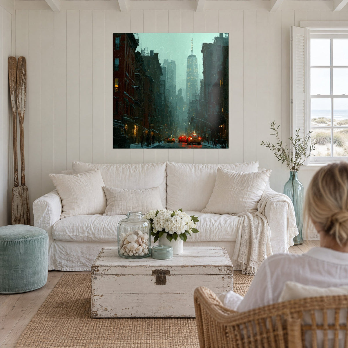 Quadro di una strada di New York sotto la pioggia, grattacieli verde acqua e facciate in mattoni rossi, due persone di spalle, sopra un divano in un soggiorno luminoso