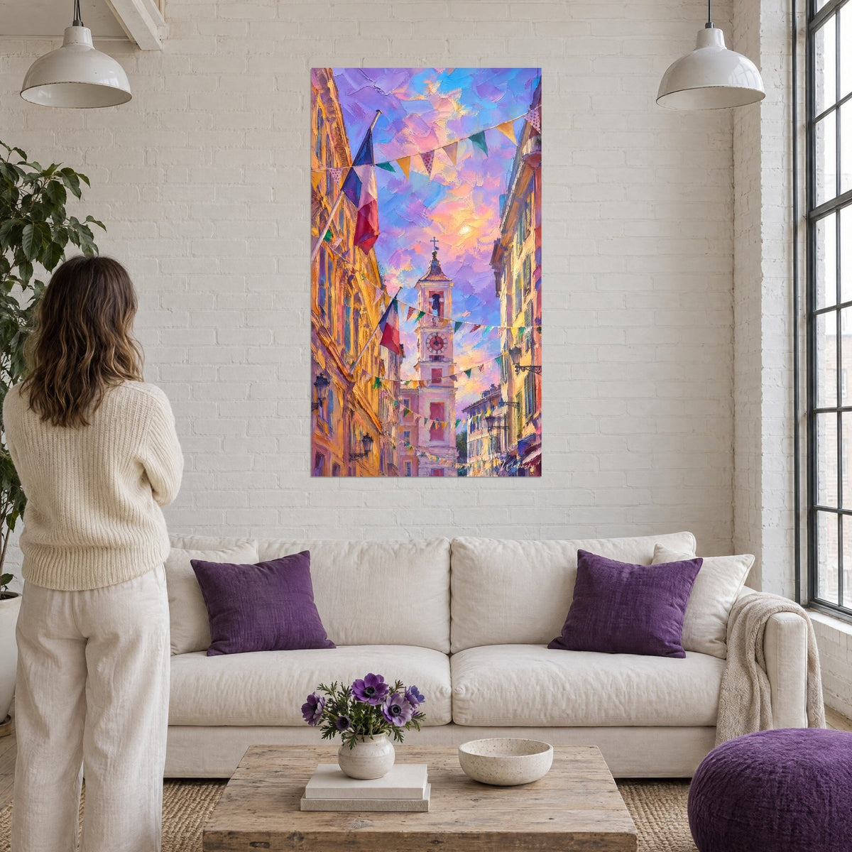 Cuadro campanario ocre bajo un cielo violeta y rosa, banderines de colores tendidos entre las fachadas, encima de un sofá en un salón luminoso