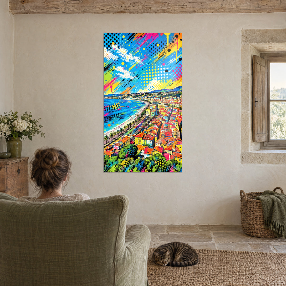 Wall art panorama of the French Riviera in vivid colours, pink and yellow splashes, one person seen from behind in a green armchair and a sleeping tabby cat