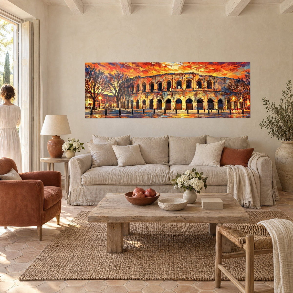 Schilderij Romeins amfitheater onder een vlammende oranje en rode hemel, okerkleurige bogen, een vrouw van achteren boven een bank in een lichte woonkamer