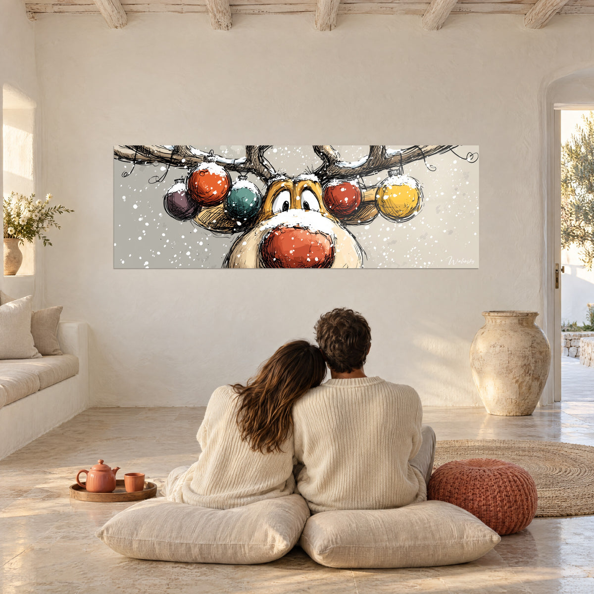 Quadro corna di renna innevate vestite di palline colorate, sfondo grigio perla, di fronte a una coppia abbracciata su cuscini bianchi