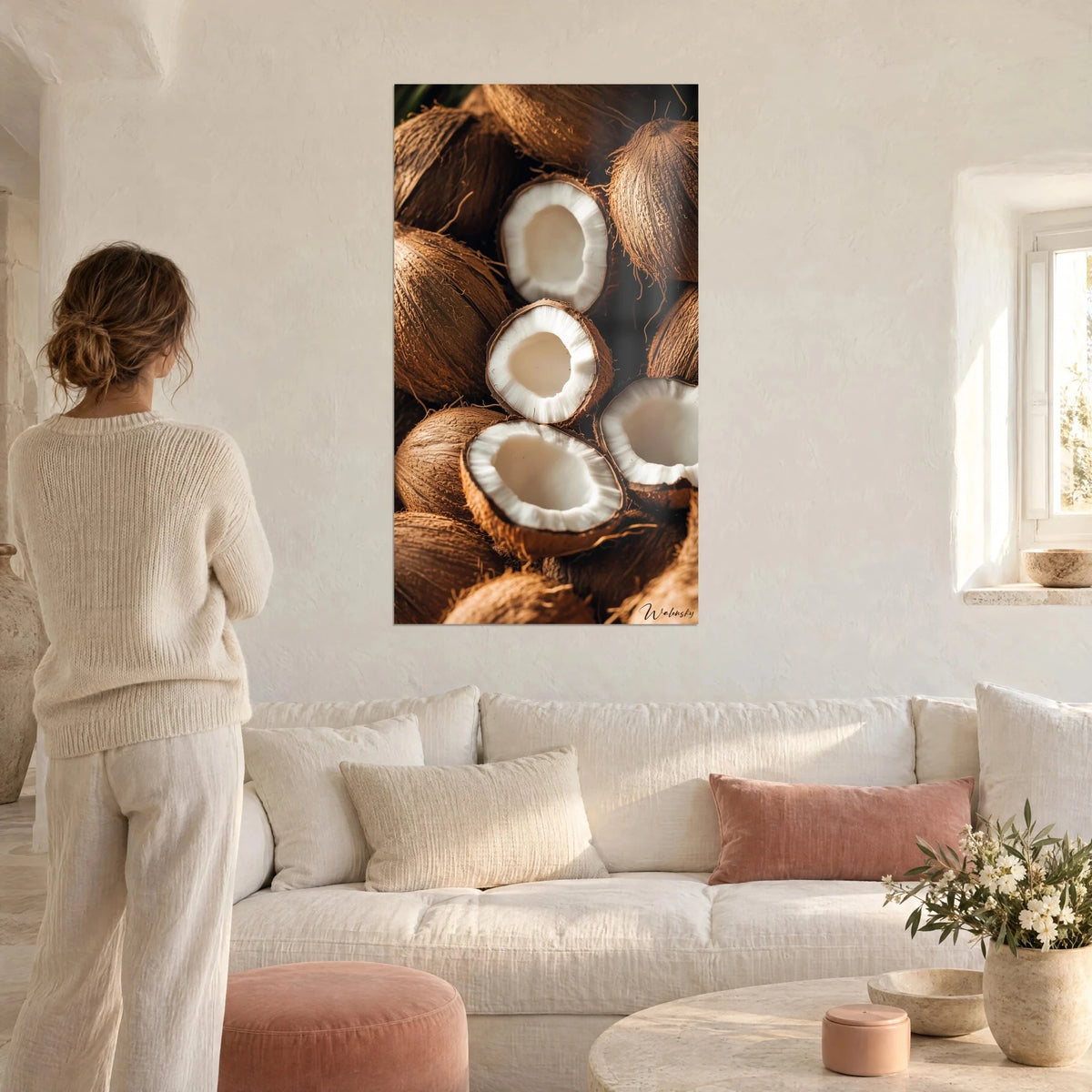 Tableau noix de coco ouvertes à chair blanche, écorce brune et poilue, face à une femme de dos, au-dessus d'un canapé dans un salon lumineux