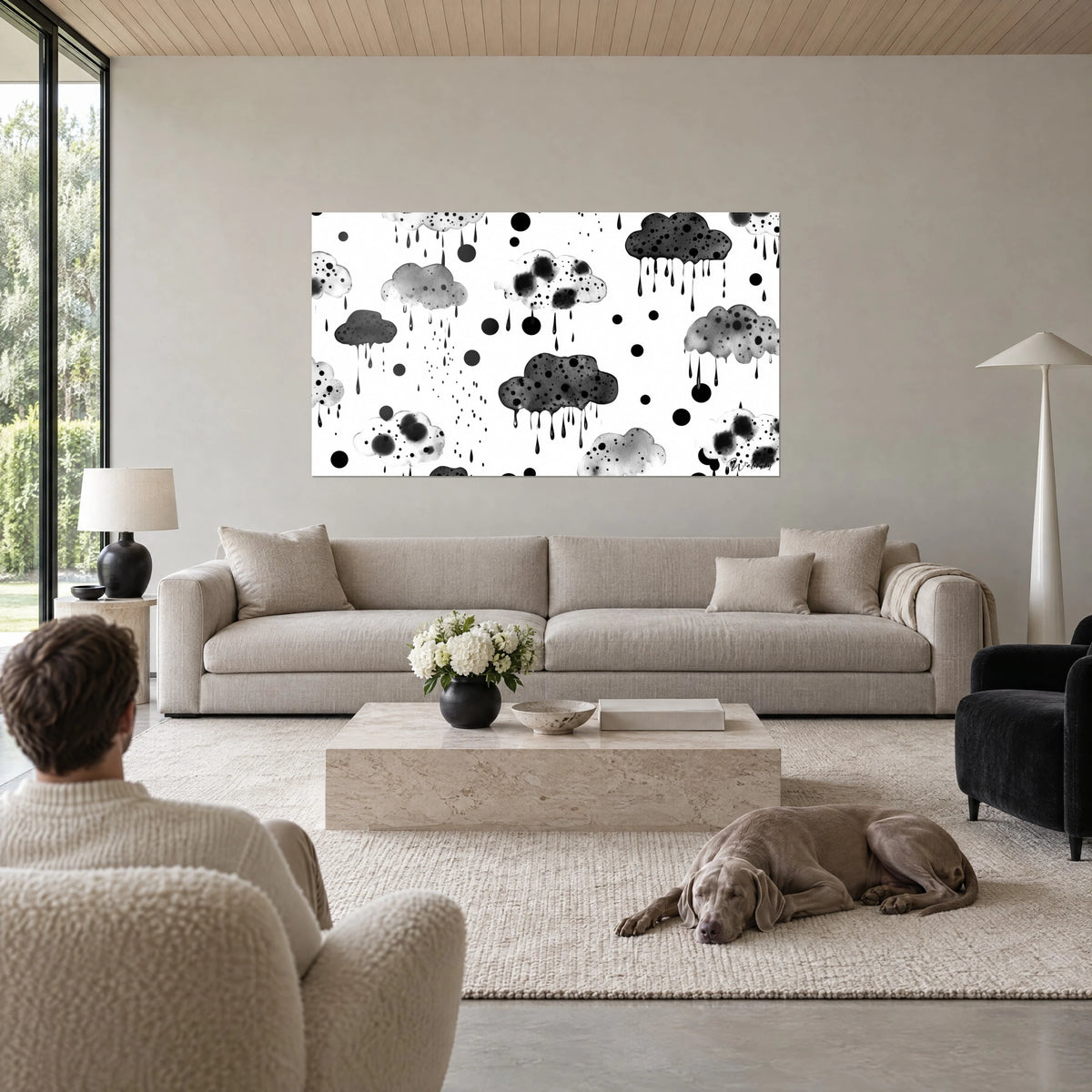 Cuadro de nubes de lluvia moteadas de negro, gotas de tinta sobre fondo blanco, dos personas de espaldas sobre un sofá en un salón luminoso