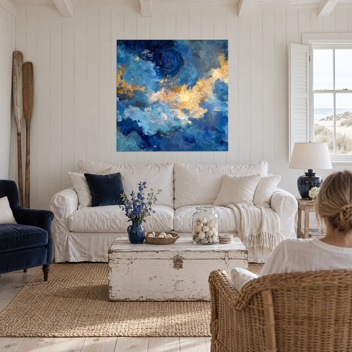 Gemälde Gewitterhimmel in Kobaltblau mit goldenen Wolkenstreifen, dunkle Spirale oben, über einem Sofa in einem hellen Wohnzimmer