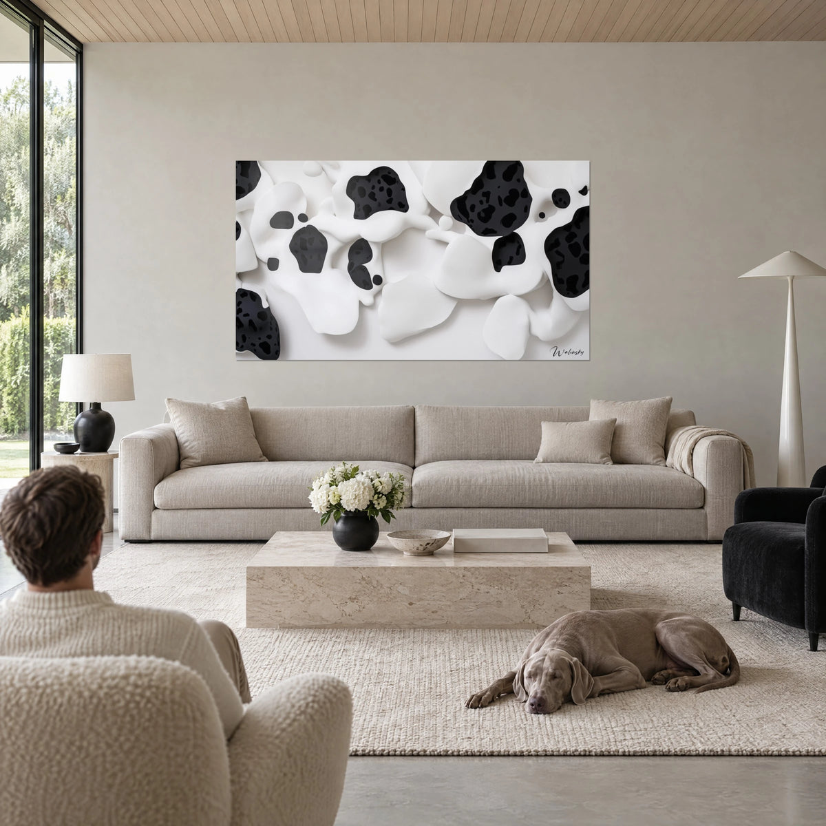Gemälde mit cremeweißen Reliefs, übersät mit schwarzen Flecken, ein Mann von hinten und ein Weimaraner über einem Sofa in einem hellen Wohnzimmer
