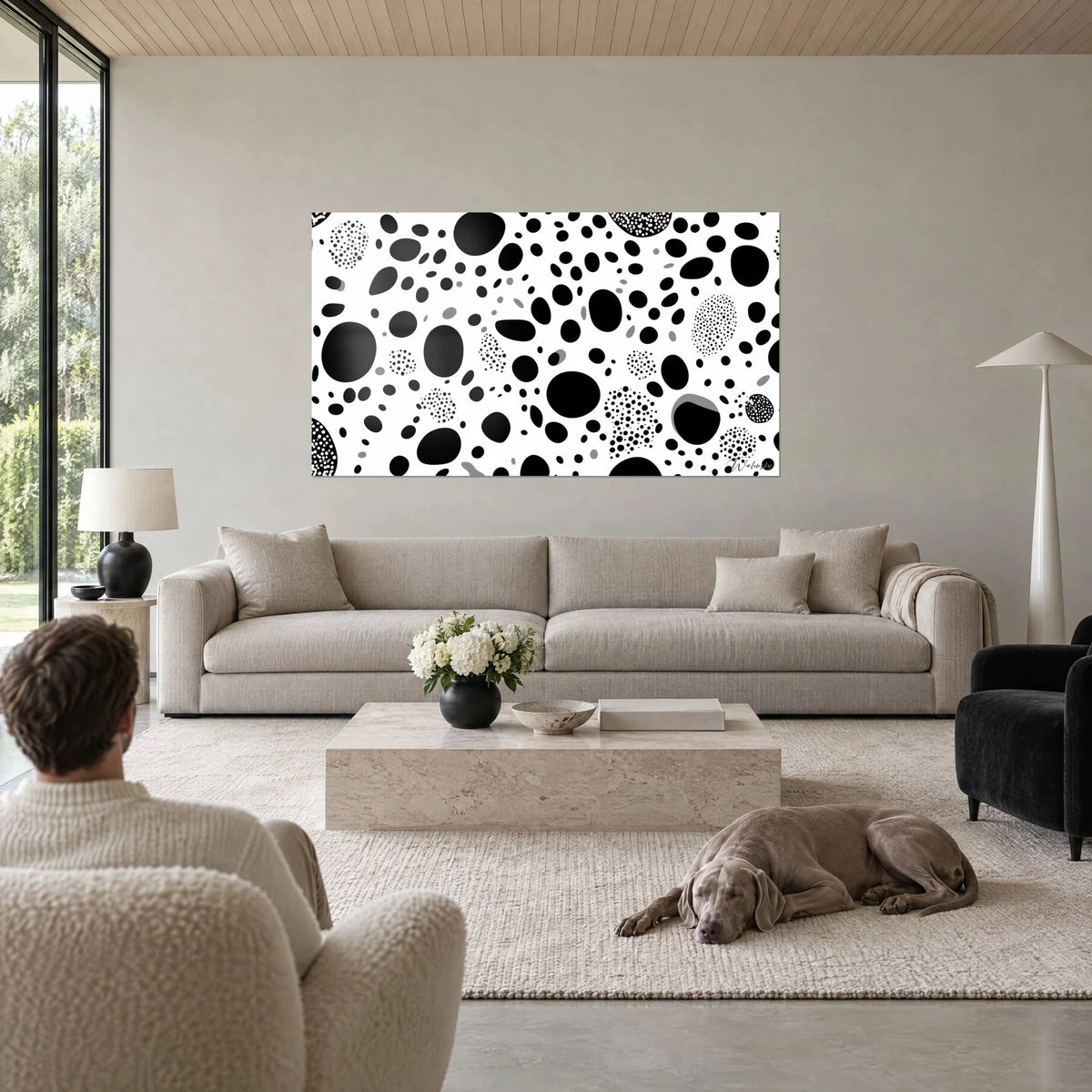Tableau taches rondes noires sur fond blanc, pois en grappes et ovales gris, au-dessus d'un canapé dans un salon lumineux