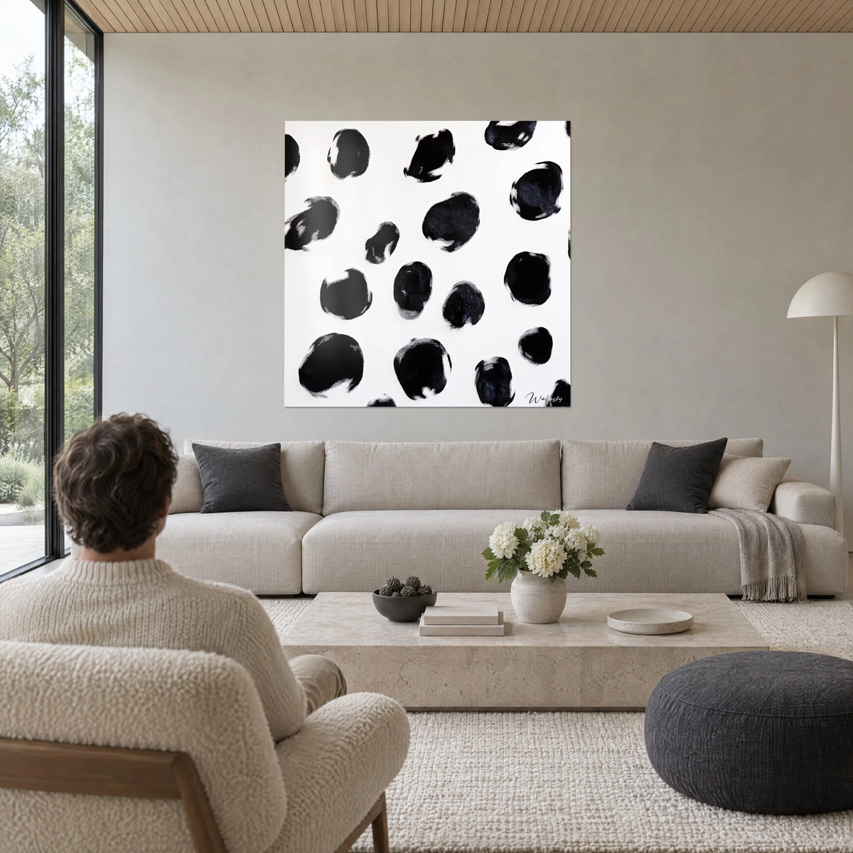 Wall art with black ink splashes on ivory background, grainy contours, a man seen from behind, above a sofa in a bright living room
