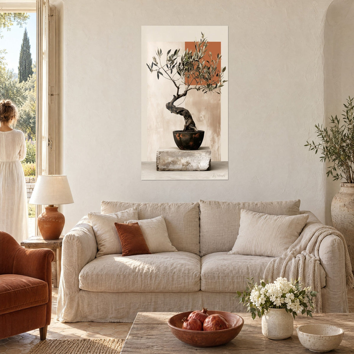 Wall art gnarled olive tree in a terracotta pot in front of a rust-coloured square and a beige wall, woman seen from behind, above a sofa in a bright living room