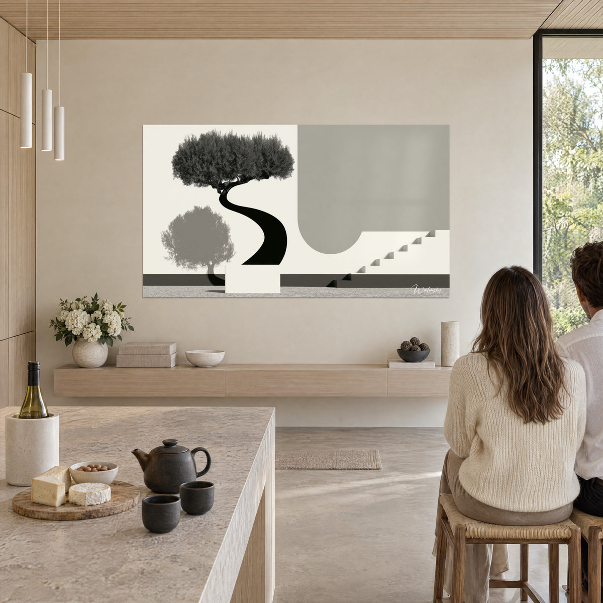 Tableau bonsaï noir au tronc ondulant et marches anthracite, accroché au mur beige d'une cuisine ouverte, deux personnes de dos