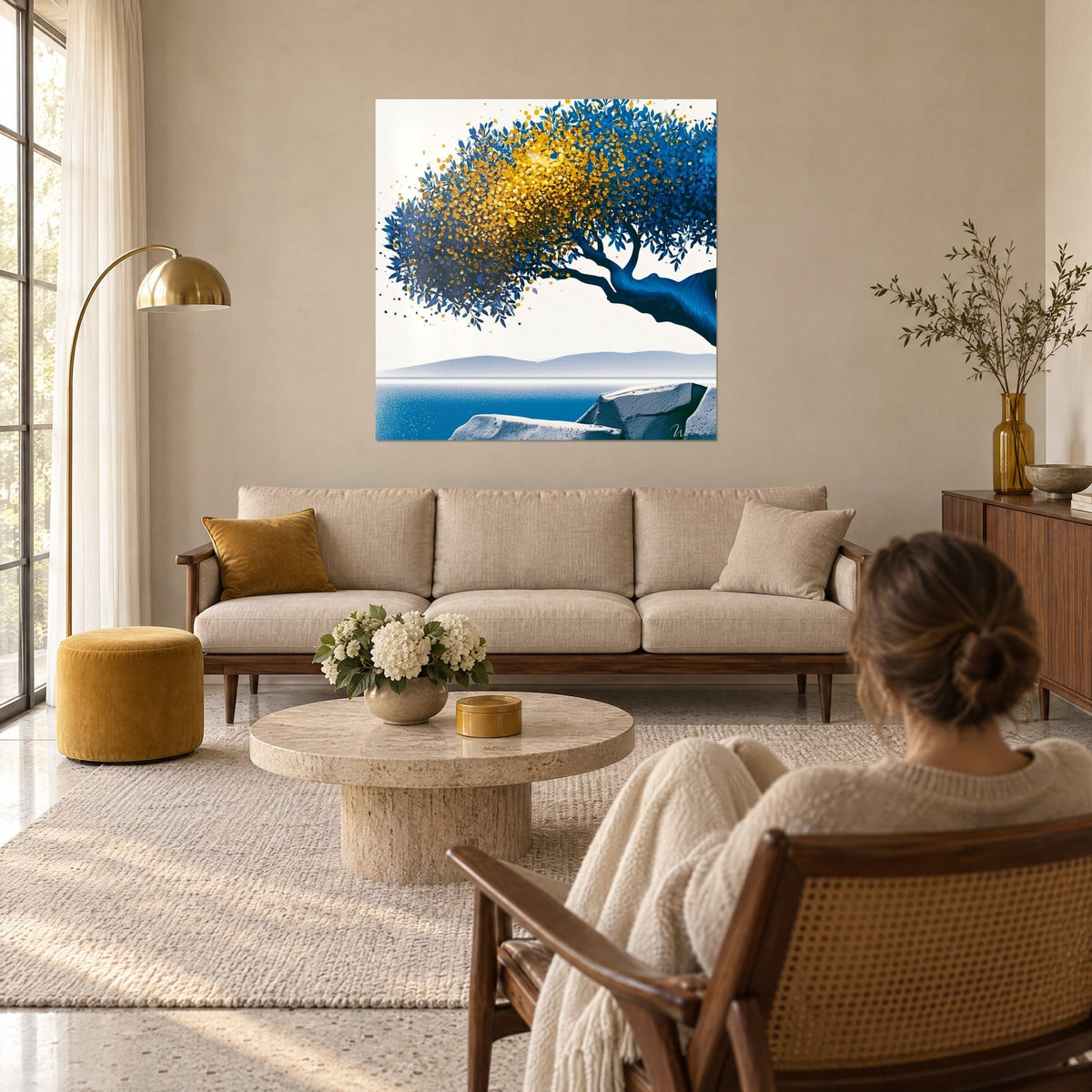 Quadro di un ulivo inclinato con fogliame blu cobalto punteggiato d'oro, mare turchese e rocce grigie, sopra un divano in un soggiorno luminoso